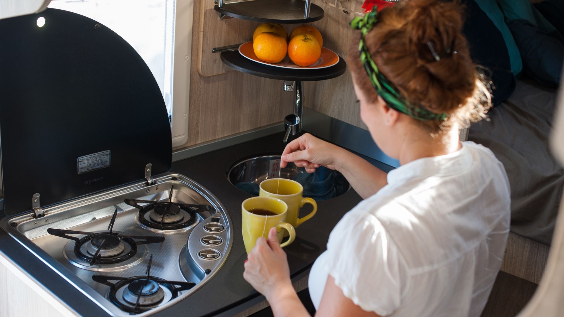 Woman preparing tea in a compact RV kitchen — The Neat Nest space-saving essentials for travel living.